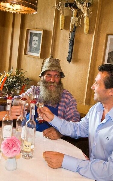 3 Personen an einem Tisch, die mit einem Glas Schnaps anstoßen