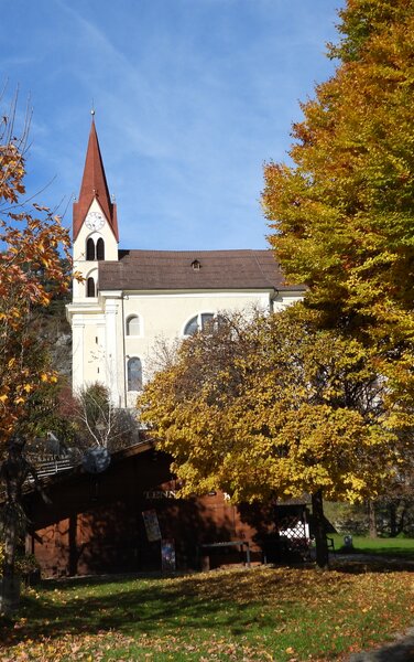 Kirche von Kiens in mitten von herbstlichen orangen Bäumen