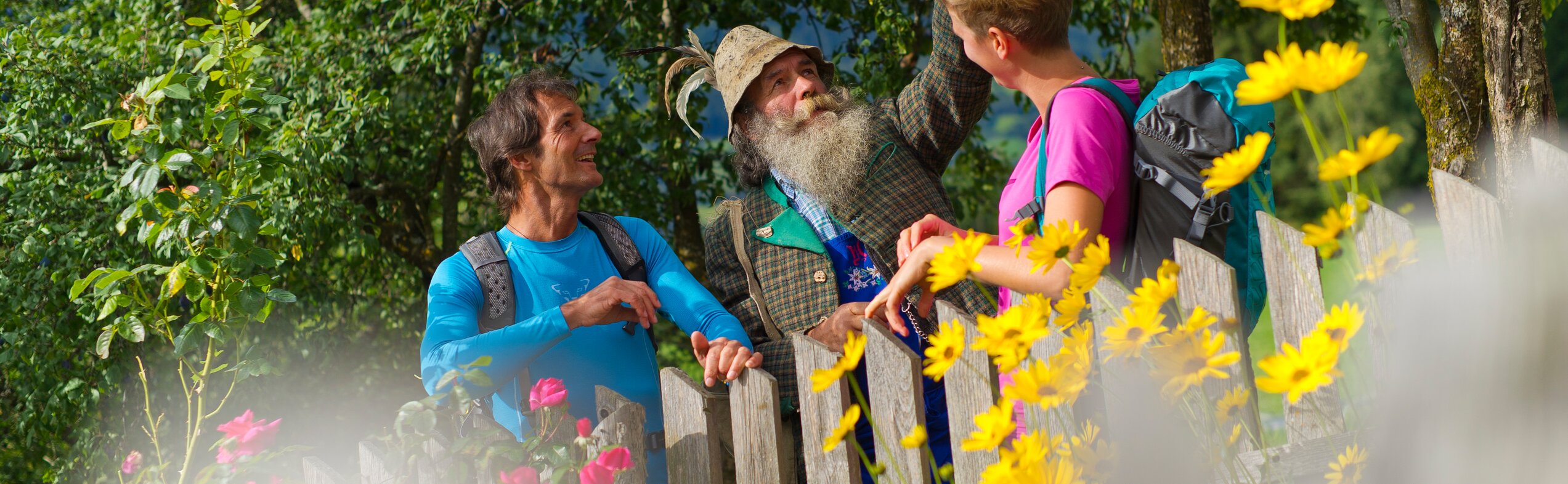 Due escursionisti con un pastore davanti a un recinto con fiori, in primavera | © Franz Gerdl