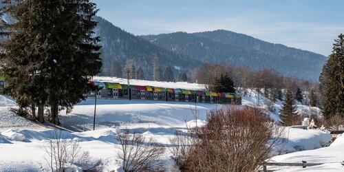 Ein Zug quert die verschneite Winterlandschaft bei strahlend blauem Himmel.