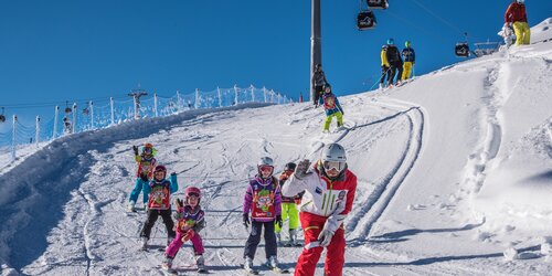 Kinder fahren mit dem Skilehrer im Kids Safety Park bei blauem Himmel. | © Skirama Kronplatz